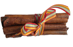 A bundle of cinnamon sticks tied with a colorful striped ribbon in red, yellow, orange, blue, and white, set against a plain white background.