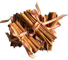 A bundle of cinnamon sticks tied with a striped ribbon in red, yellow, and white, arranged on a white textured background.