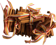 A bundle of cinnamon sticks tied with colorful striped ribbon on a white marble surface.