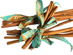 3 bundles of cinnamon sticks tied with two turquoise and orange patterned ribbon bows, placed on a white fabric background.