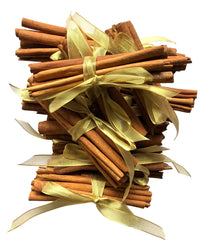 ten bundles of whole cinnamon sticks tied with sheer gold ribbon bows, arranged on a white background.
