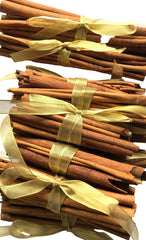 Ten bundles of cinnamon sticks tied with gold sheer ribbons, arranged diagonally on a white background.