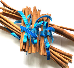 5 bundles of cinnamon sticks tied with a turquoise dotted ribbon, photographed on a plain white background.