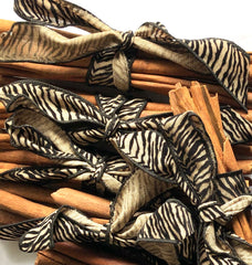 Zebra-print ribbon tied in bows over cinnamon sticks on a white background.