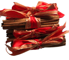 five bundled sticks of cinnamon tied with red and gold glitter ribbon bows, arranged on a white surface.